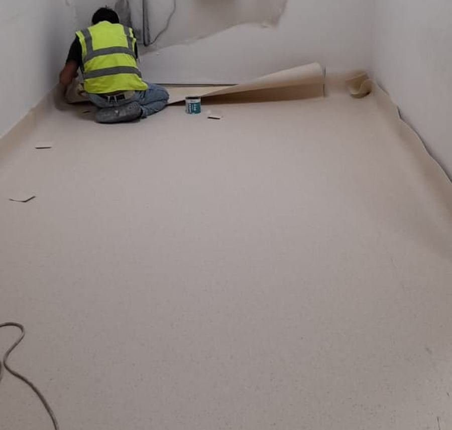 Eco Formax technician dressing medical-grade sheet vinyl to the wall in a clinical room
